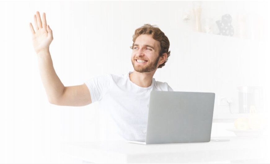 A smiling trader waving from behind a laptop.